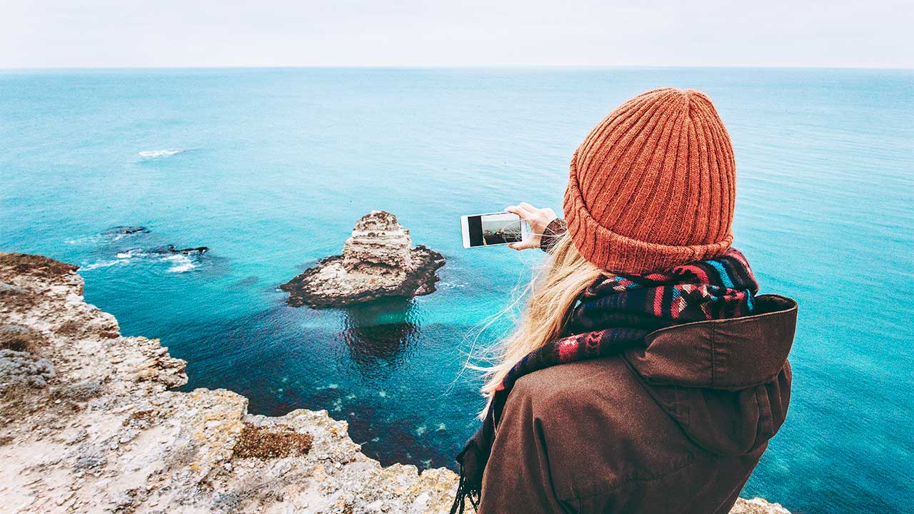 junge Frau fotografiert mit dem Smartphone eine Küstenlandschaft