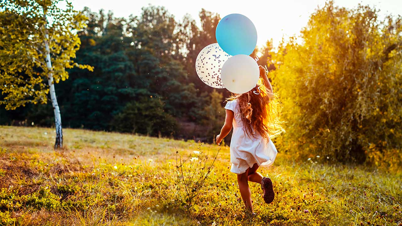 Mädchen rennt mit Ballonen über eine Wiese