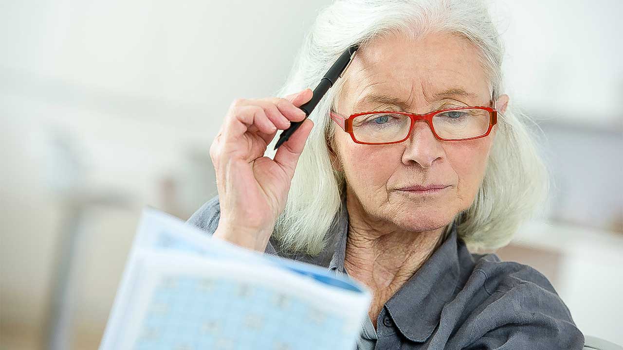 Ältere Frau mit Brille überlegt und hält ein Dokument in Händen