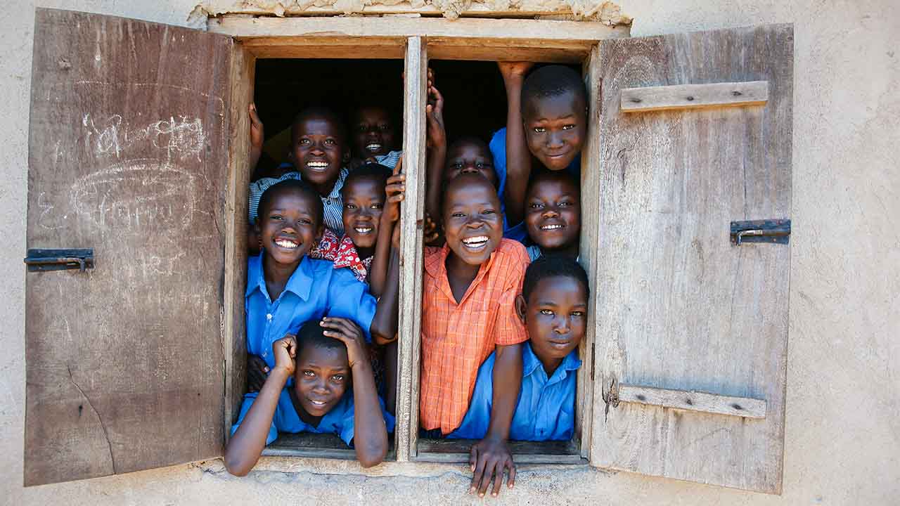 Kinder in Uganda blicken fröhlich aus einem Fenster