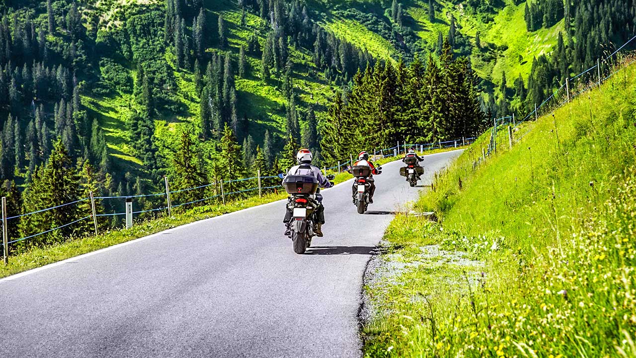 Drei Motorradfahrer unterwegs auf einer Bergstrasse in den Alpen