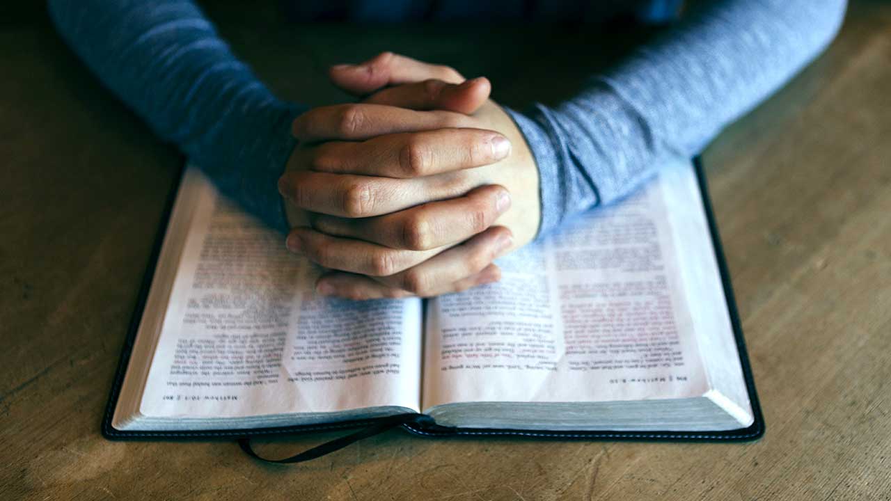 Gefaltete Hände beim Gebet auf einer Bibel