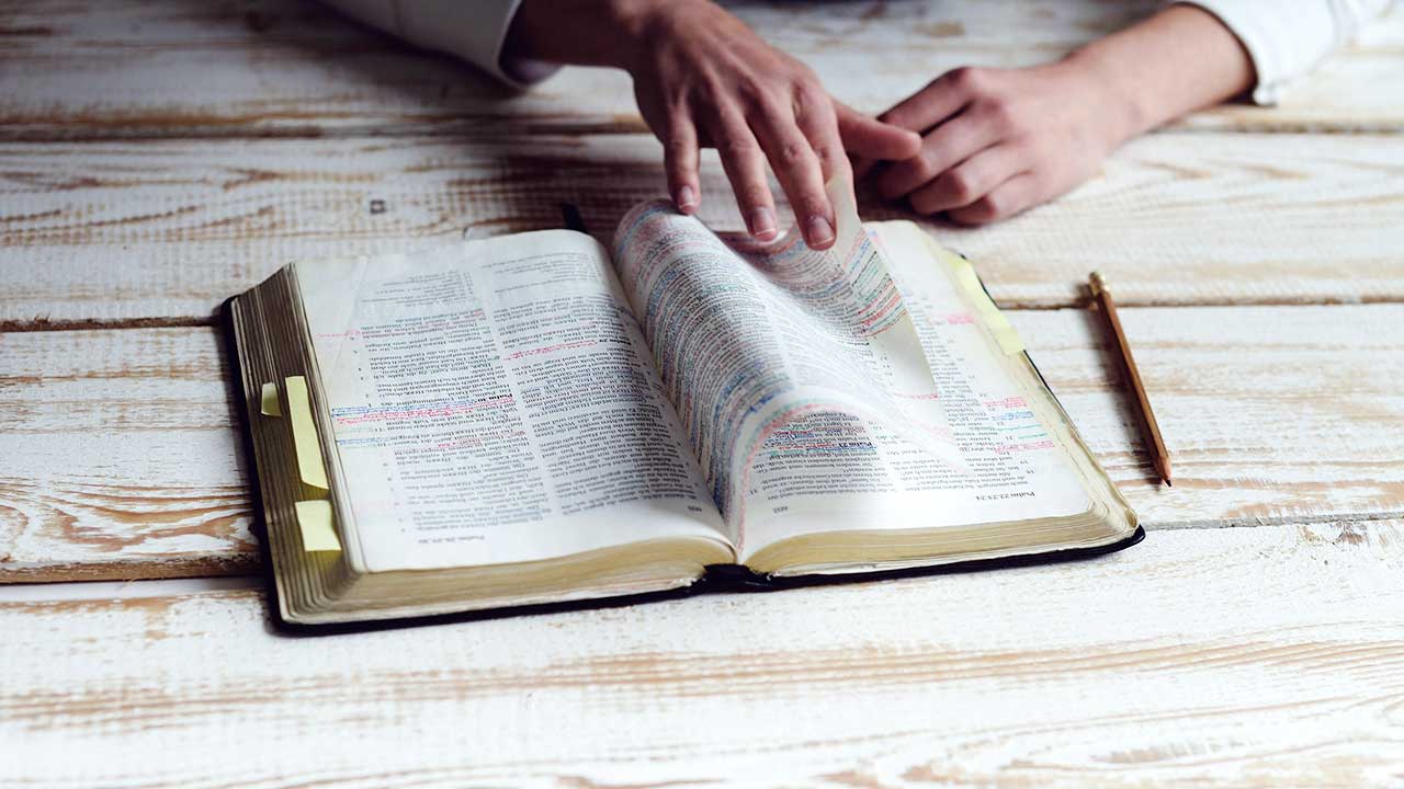 Aufgeschlagene Bibel auf einem Holztisch, eine Hand blätter darin