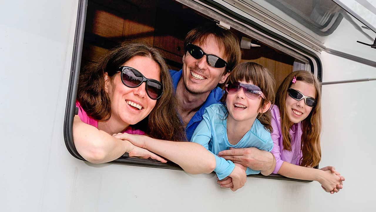 vierköpfige Familie blickt aus dem Fenster eines Camping-Wagens