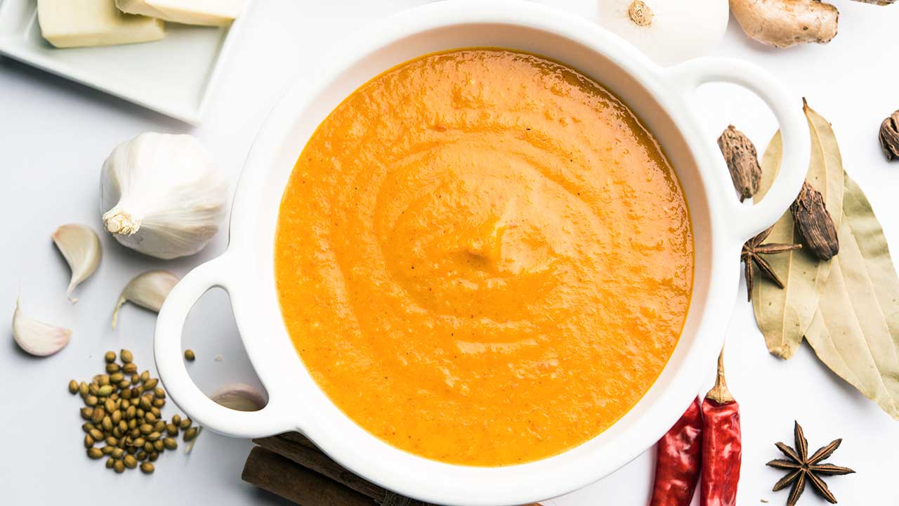 Currysuppe in einer weissen Schüssel, darum herum Zutaten