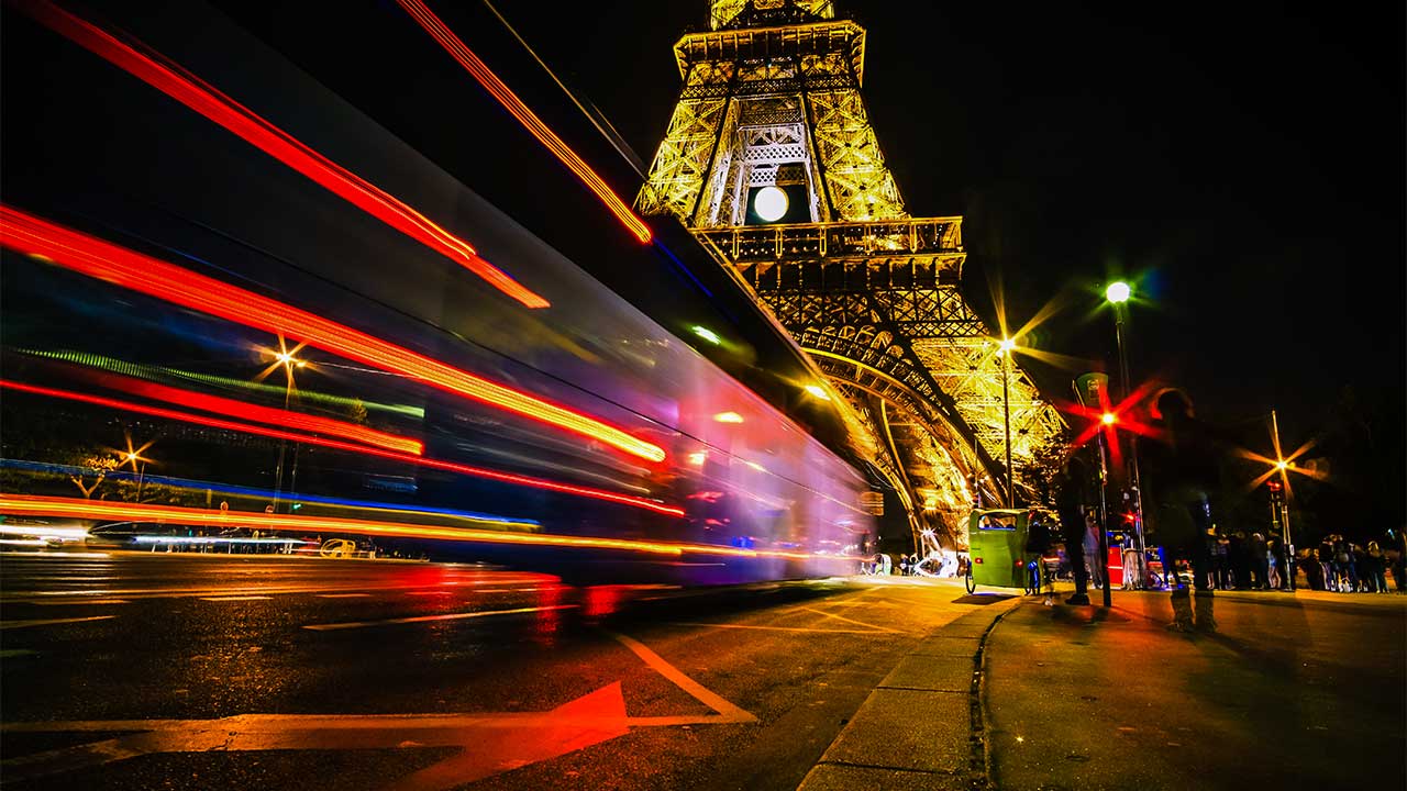 beleuchteter Eiffelturm nachts in Paris, mit Lichtspuren von Autos
