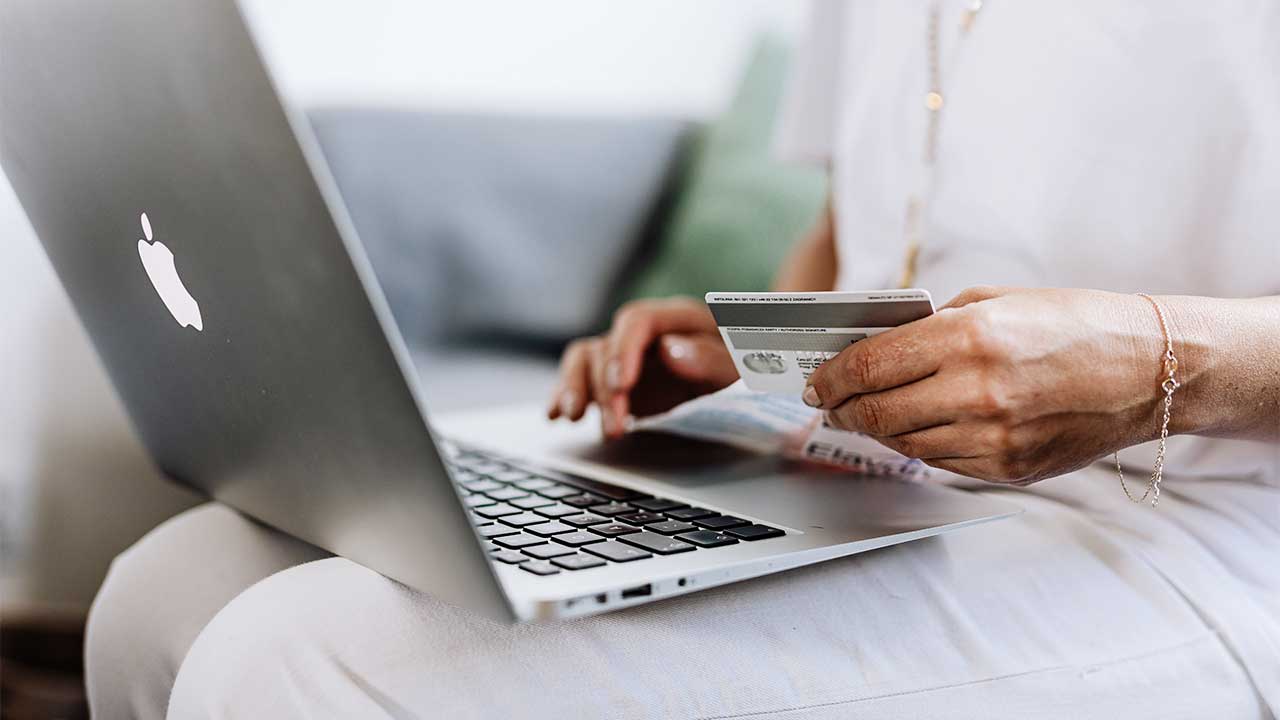 Online-Shopping: Frauenhände mit einer Kreditkarte, auf dem Schoss ein Laptop