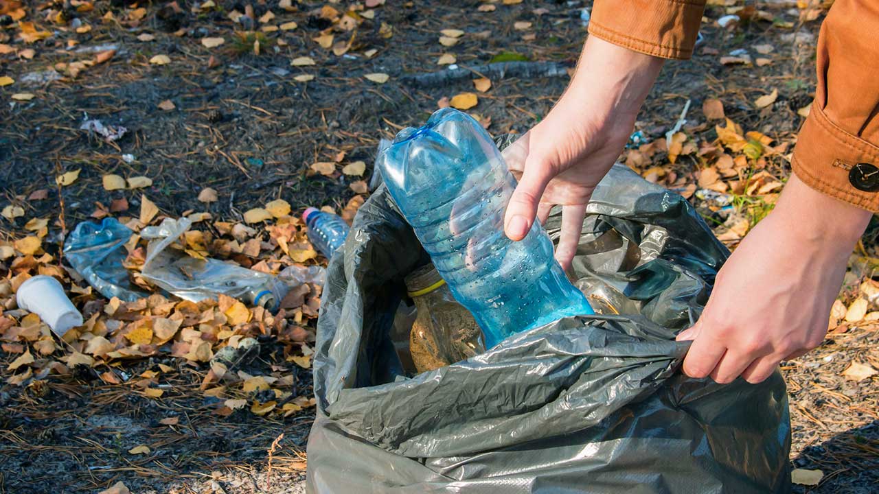 Hände werfen eine Plastikflasche in einen Abfallsack