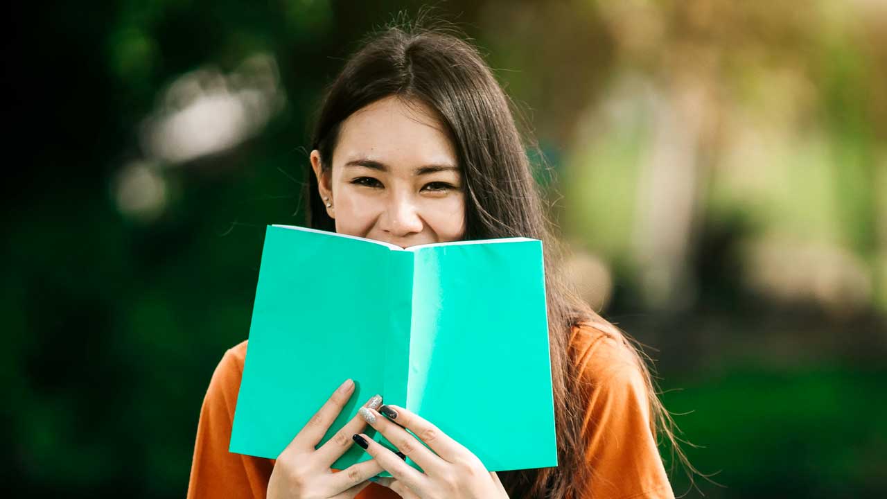 Junge Frau hält Buch vor ihren lachenden Mund