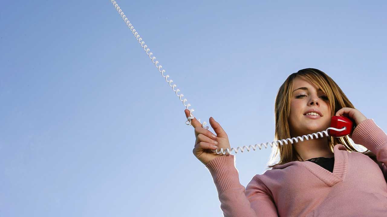 Frau hält einen Telefonhörer in der Hand, dessen Kabel in den Himmel reicht