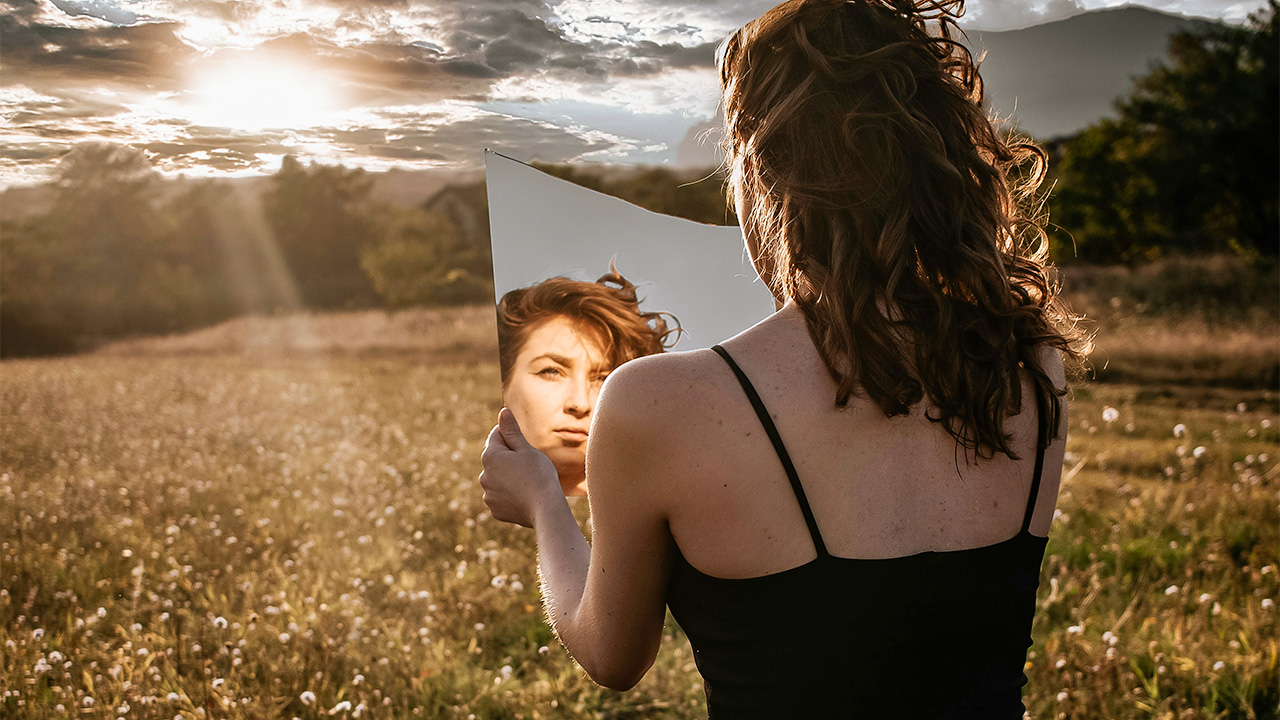 Frau blickt auf einem freien Feld in einen Spiegel