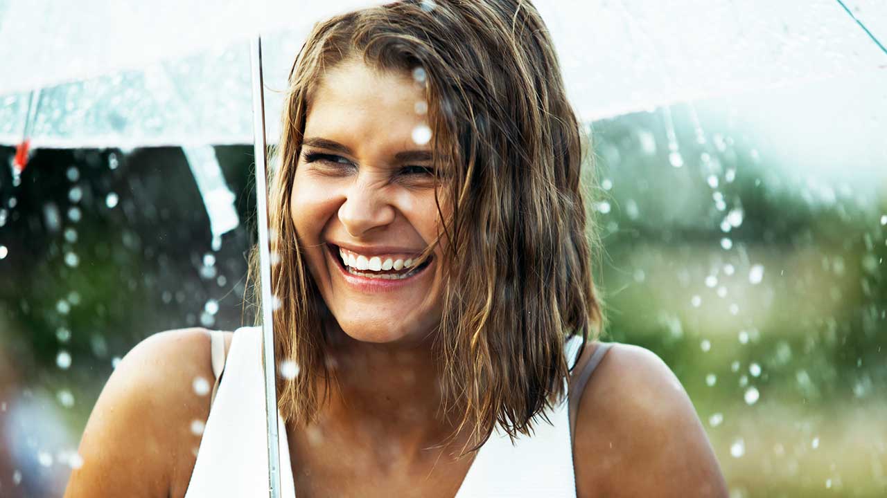 Frau lächelt unter einem Schirm bei Regen