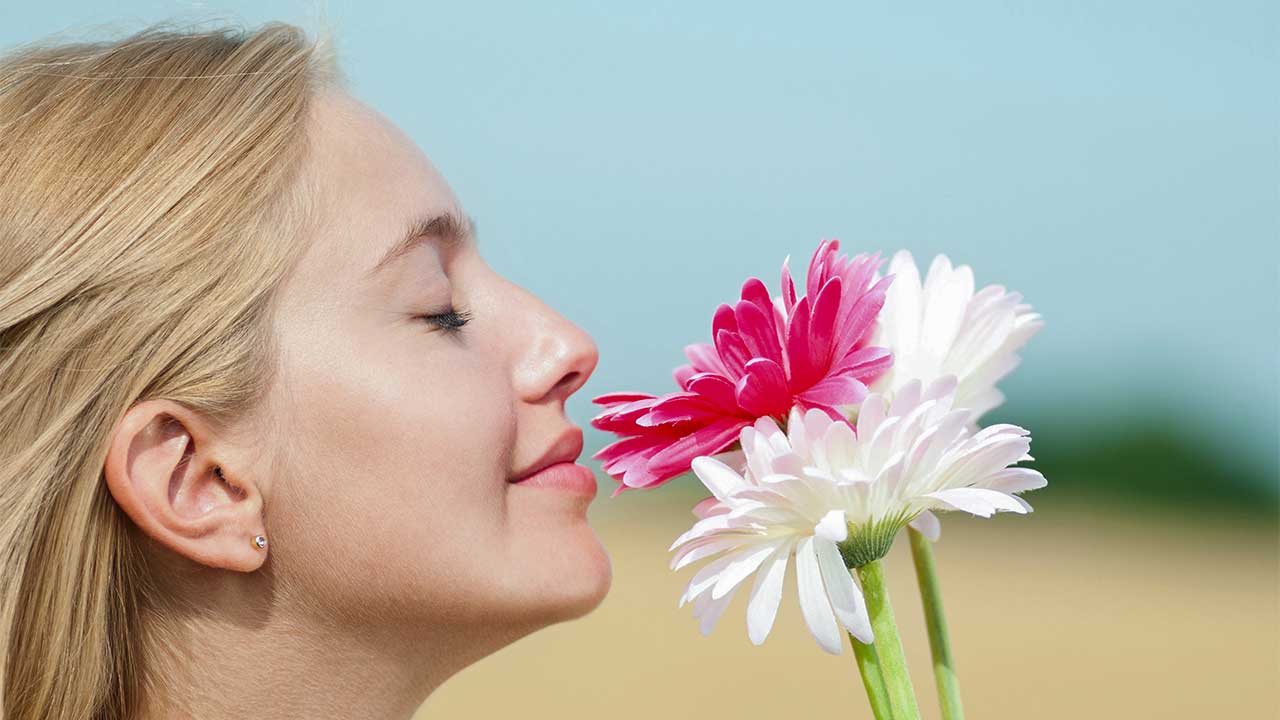 junge Frau riecht mit geschlossenen Augen an roten und weissen Blumen