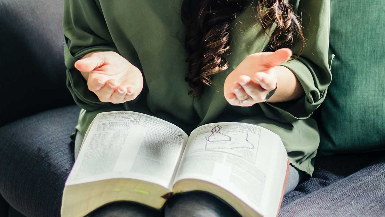 Hände einer Frau, welche betend über einer Bibel sind