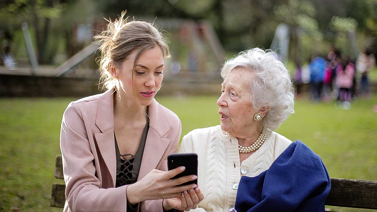 junge und ältere Frau auf einer Parkbank mit einem Smartphone