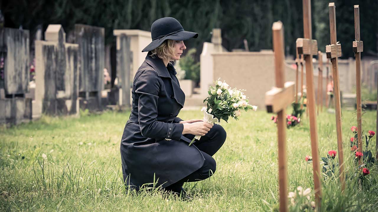 Frau knied vor einem Holzkreuz auf einem Friedhof