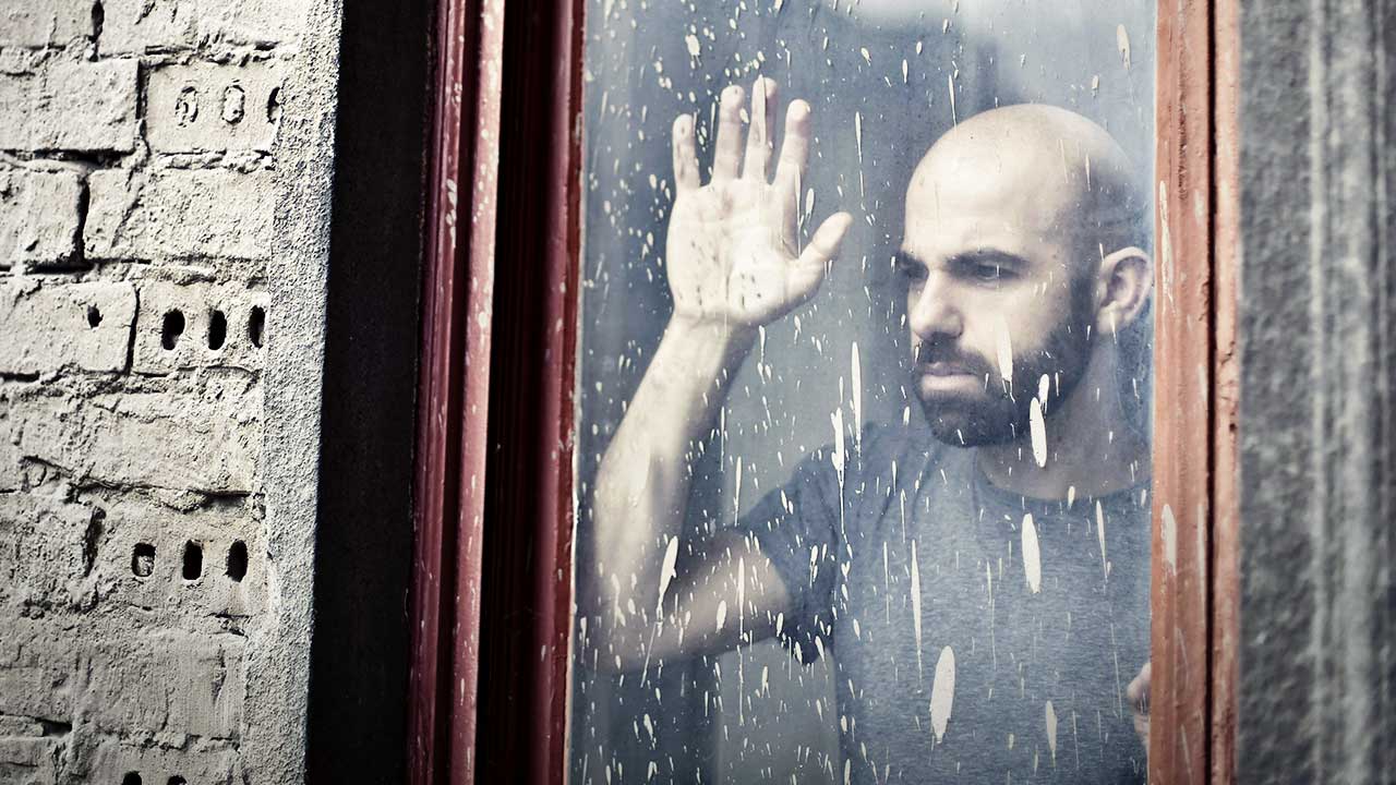 Mann blickt ernst durch ein verdrecktes Fenster