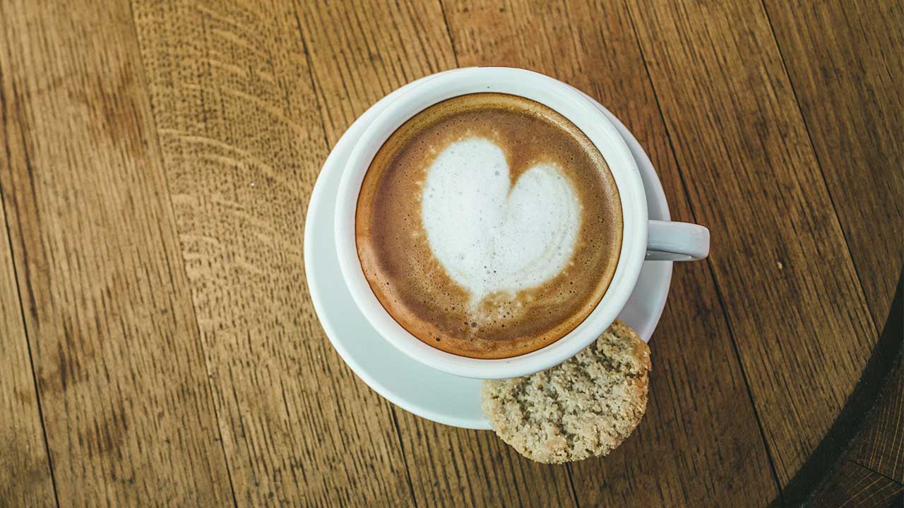 Tasse mit Kaffee auf einem Holztisch, der Schaum hat die Form eines Herzens