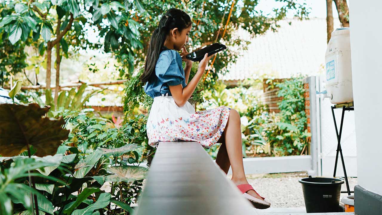 Mädchen in Indonesien sitzt auf einer Veranda und hantiert mit einem Smartphone