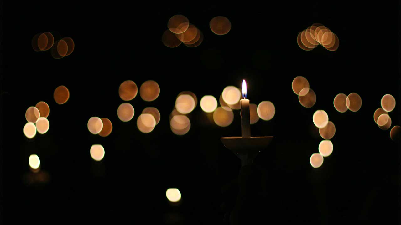 Brennende Kerze mit Lichterflecken im Hintergrund
