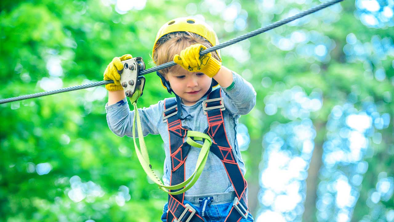 Junge klettert an einem Seil, mit einem Sicherheitsgurt abgesichert