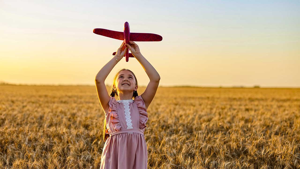 Mädchen steht in einem Getreidefeld und hält ein Modellflugzeug in die Luft