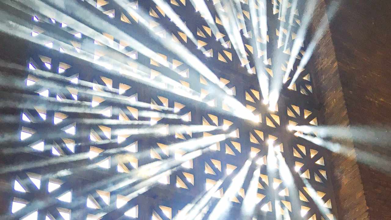 Sonnenstrahlen dringen durch das Gitterfenster eines Kirchengebäudes