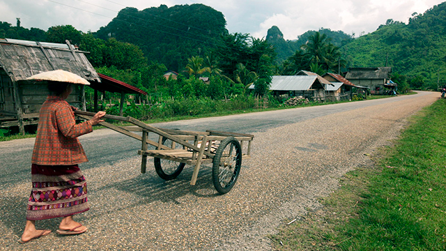 Frau mit Schubkarren in einem laotischen Dorf