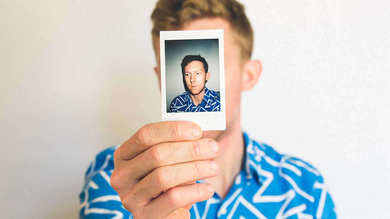 Mann hält Polaroid-Foto von sich vor sein Gesicht