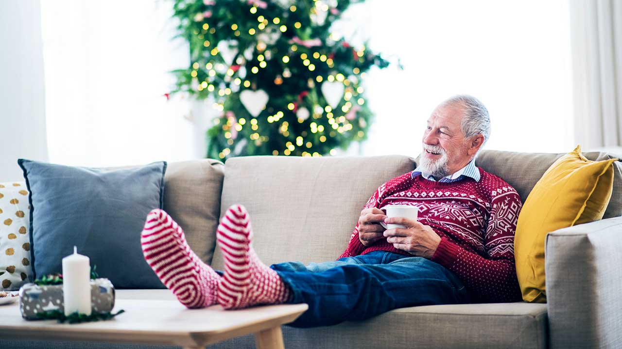 Mann sitzt zufrieden auf dem Sofa, im Hintergrund ein Weihnachtsbaum
