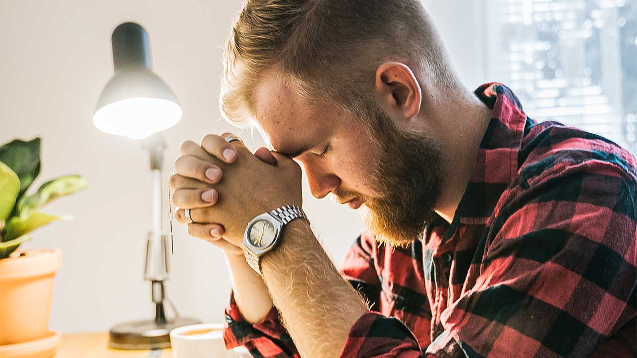 Mann sitzt an einem Tisch und betet konzentriert