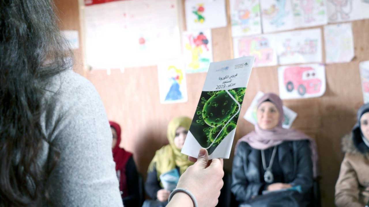 Medair-Mitarbeiterin mit einer Broschüre über Virus vor einer Frauengruppe