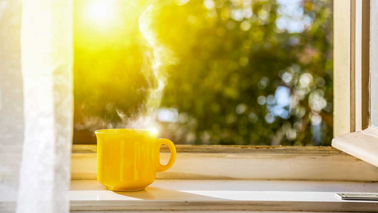 Offenes Fenster mit gelber Tasse und Sonnenschein