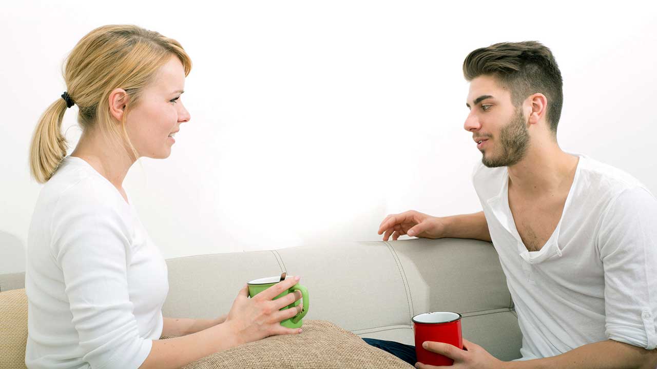 Ein junges Paar sitzt auf dem Sofa, mit Tassen in den Händen und führt ein Gespräch