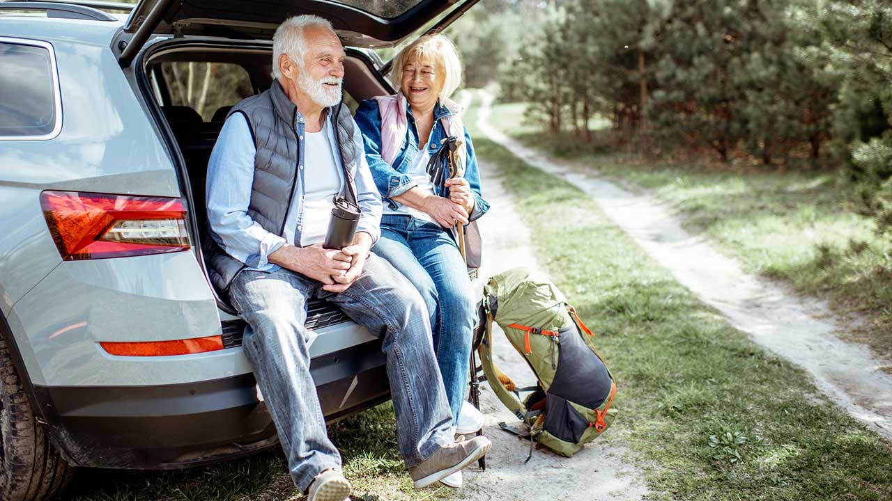 Seniorenpaar auf Reise sitzt im offenen Kofferram und macht Pause