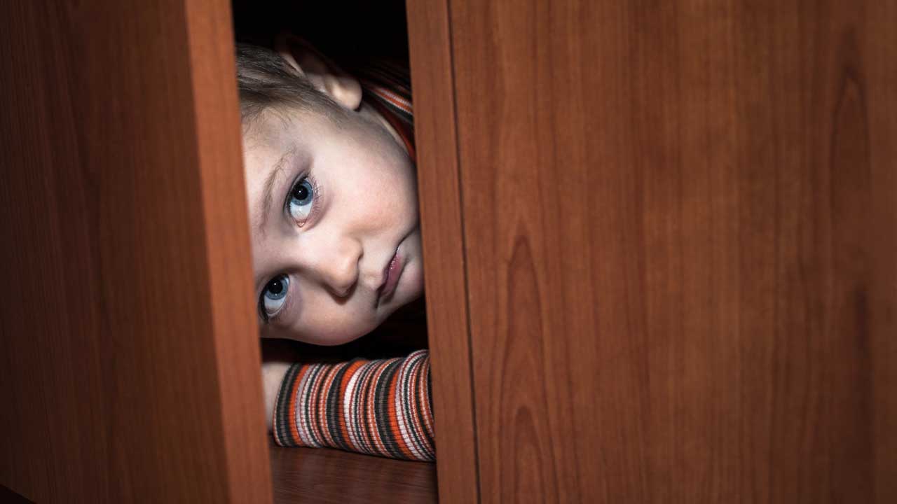 Kind hat sich im Schrank versteckt und blickt aus der offenen Tür hervor