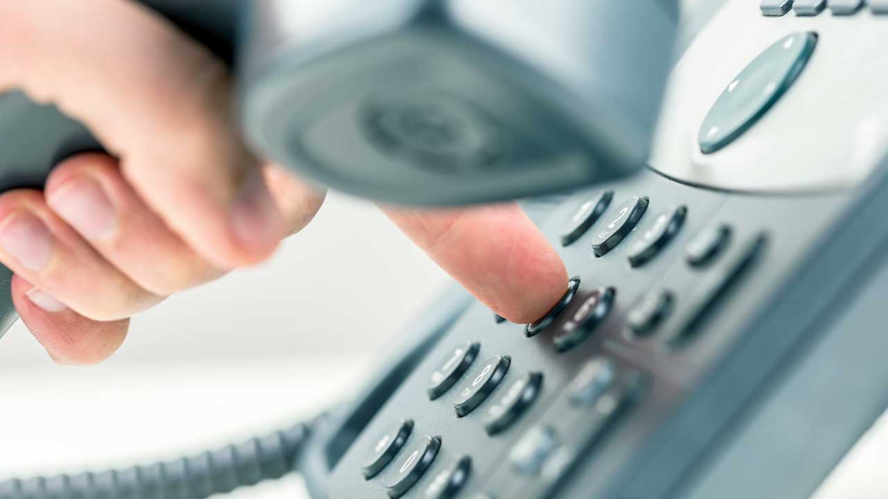 Eine Hand mit einem Telefonhörer wählt eine Nummer