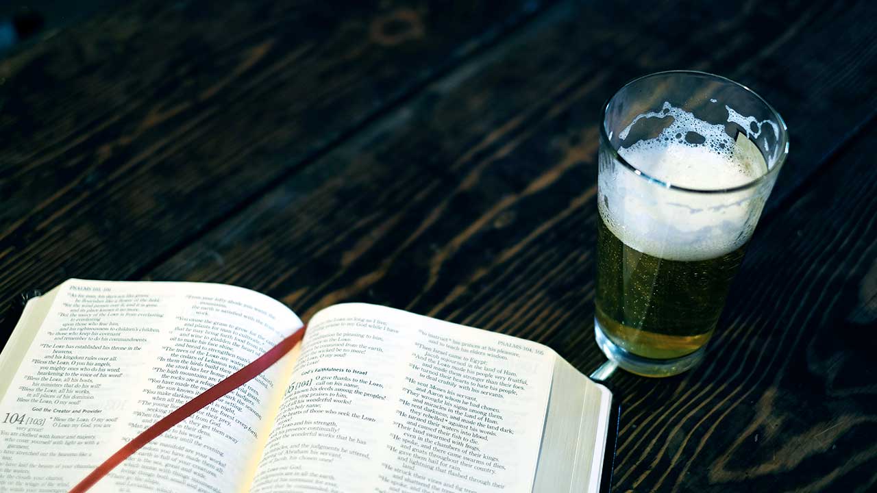 offene Bibel und Glas mit Bier auf einem Holztisch