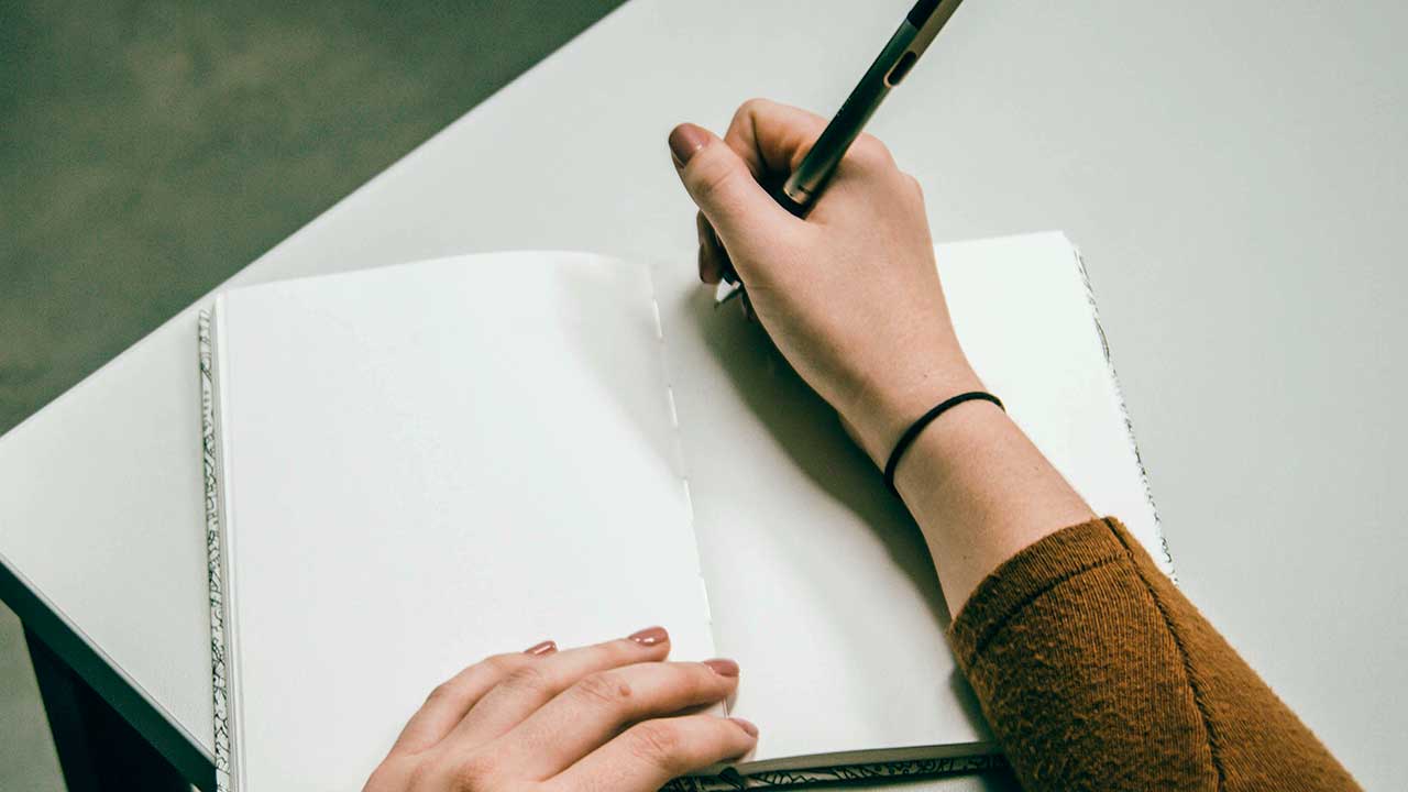 Hand mit Kugelschreiber beginnt in ein Notizbuch zu schreiben