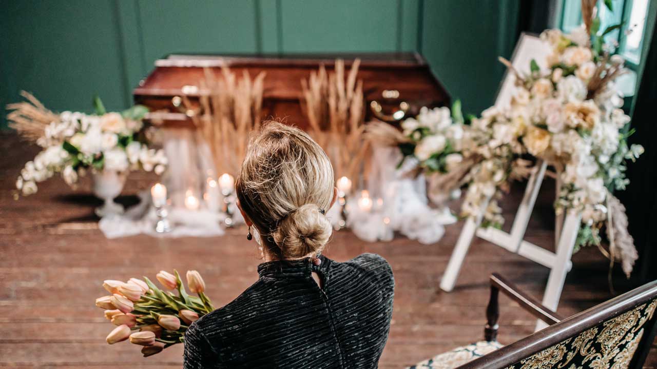 Rückansicht auf eine trauernde Frau vor einem Sarg mit Blumen