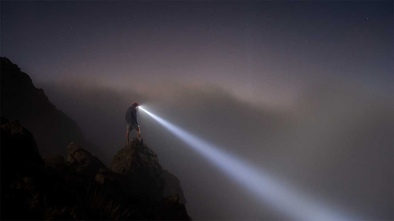 Mann steht auf einem Berg und leuchtet mit seiner Helmlampe abwärts