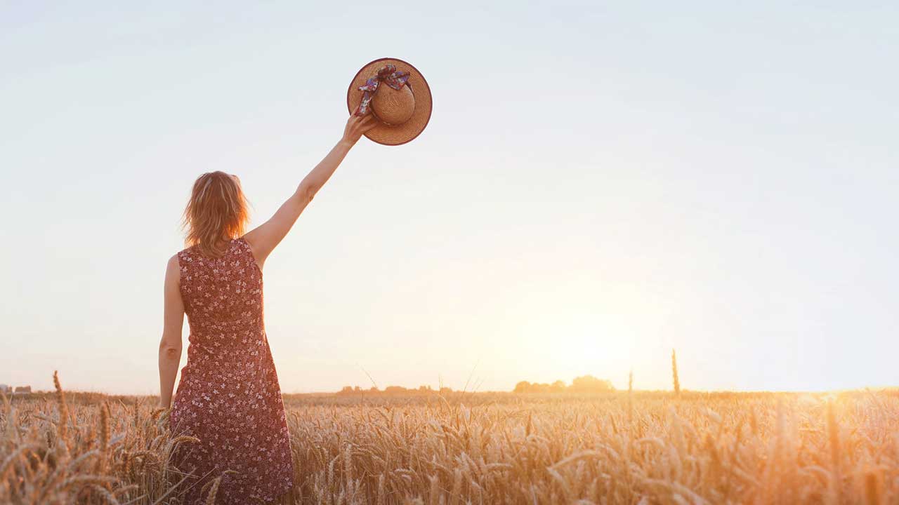 In einem Getreidefeld winkt eine Frau mit ihrem Hut zum Abschied