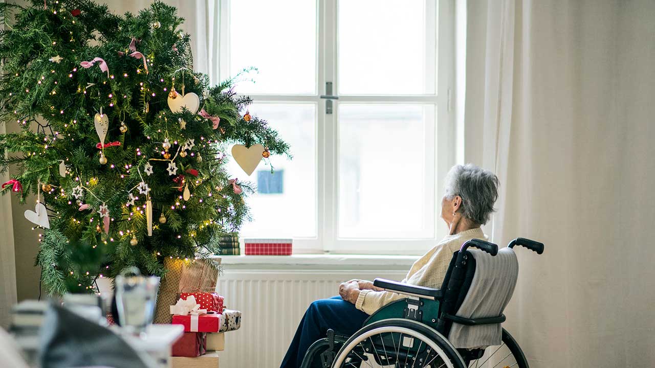 Seniorin im Rollstuhl sitzt allein vor einem Christbaum