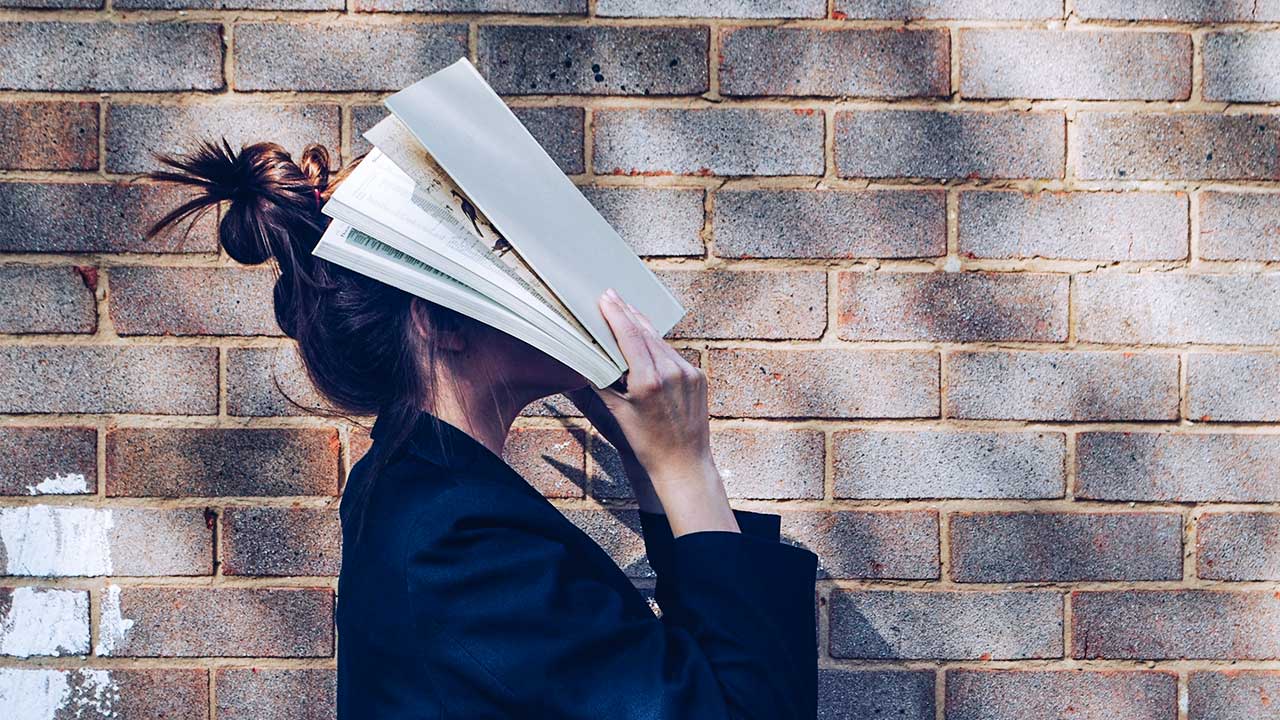 junge Frau verdeckt ihr Gesicht mit einem offenen Buch