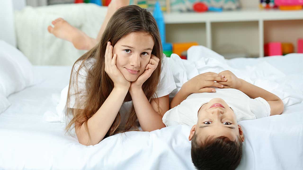 Schwester und Bruder auf einem Bett im Kinderzimmer