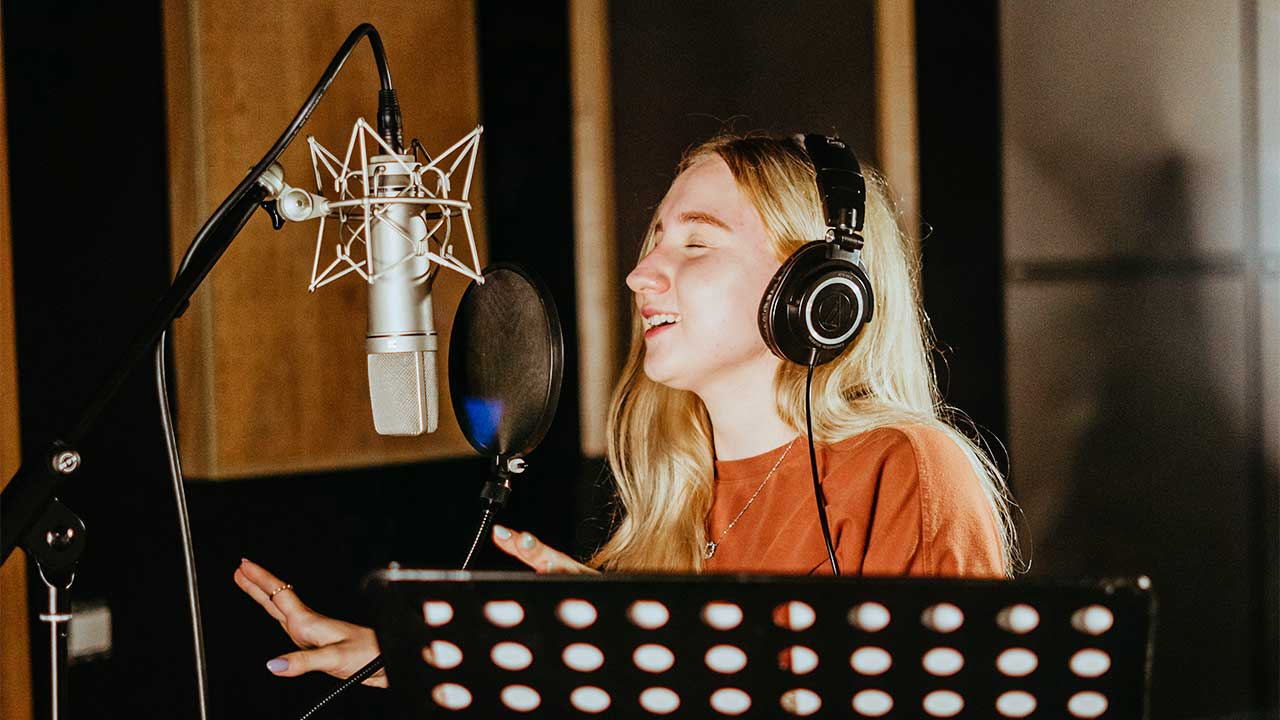 junge Frau steht in einem Studio und singt in ein Mikrofon
