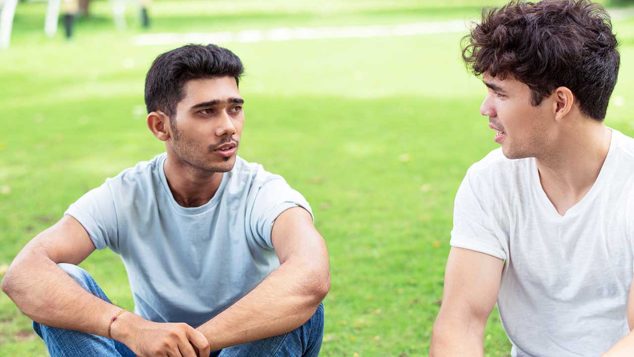 Zwei junge Männer sitzen auf einer Wiese und sind im Gespräch