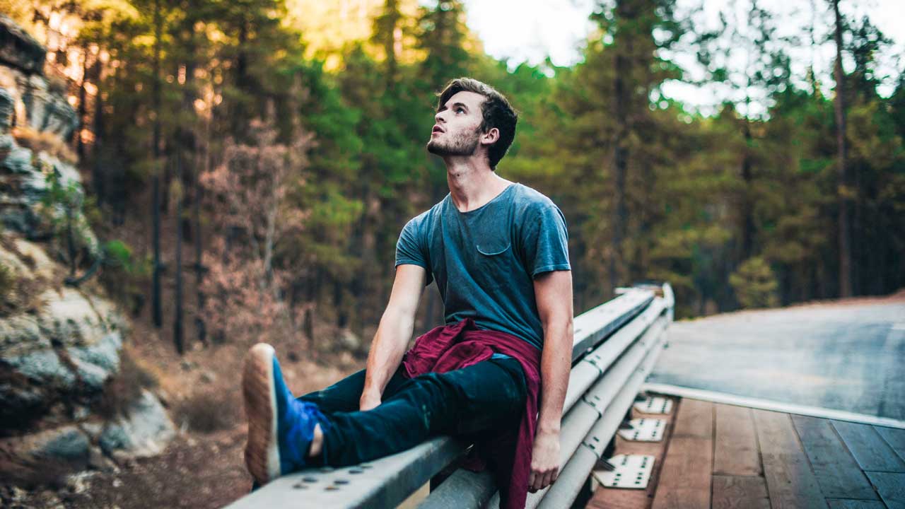junger Mann sitzt auf einem Geländer und blickt nach oben