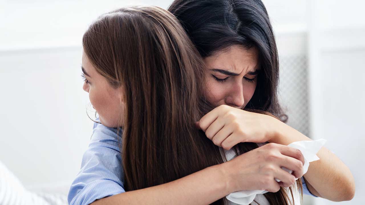 eine junge Frau umarmt eine andere, welche weint